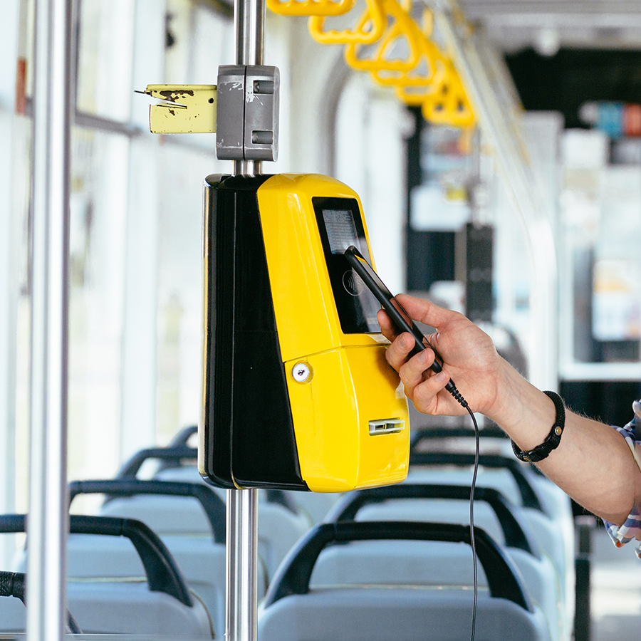 Main tenant un smartphone devant un validateur de titre de transport pour paiement sans contact.
