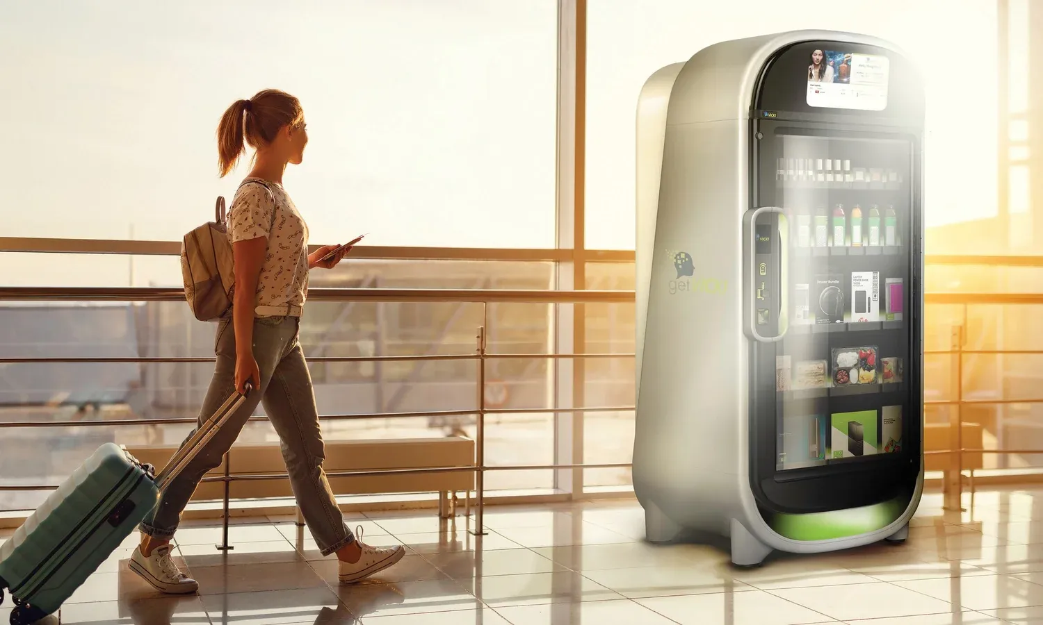 A traveler with a rolling suitcase walks past a VICKI smart store in a sunlit airport terminal.