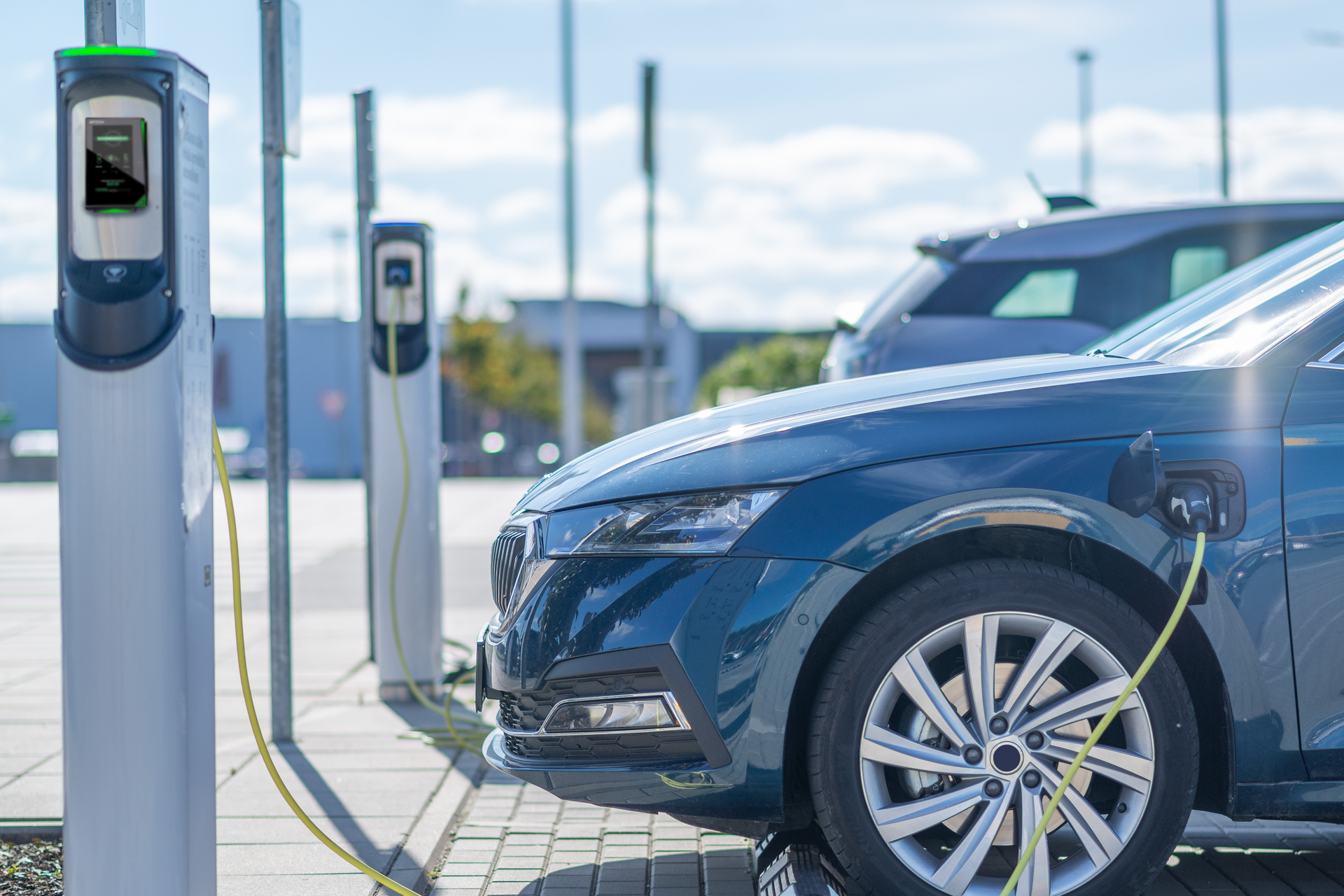 An electric car plugged into an outdoor EV charging station equipped with a payment reader.